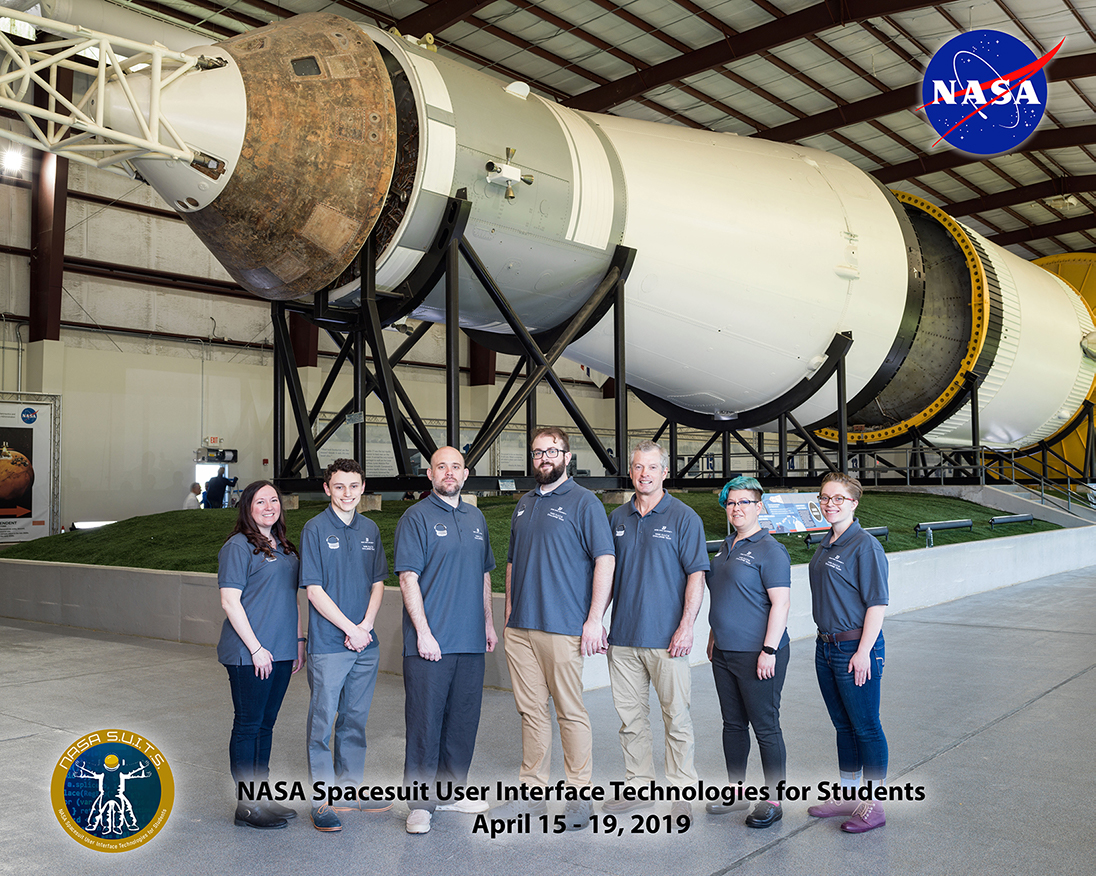 Boise State University NASA SUITS Onsite Team Photo in front of the Saturn IV Rocket in Rocket Park. Left to Right: Dr. Karen Doty, Dean Cohen, Daniel Lambert, Taylor Campbell, Ret. NASA Astronaut Steve Swanson, Liz Altmiller, and Brenna Leonard.